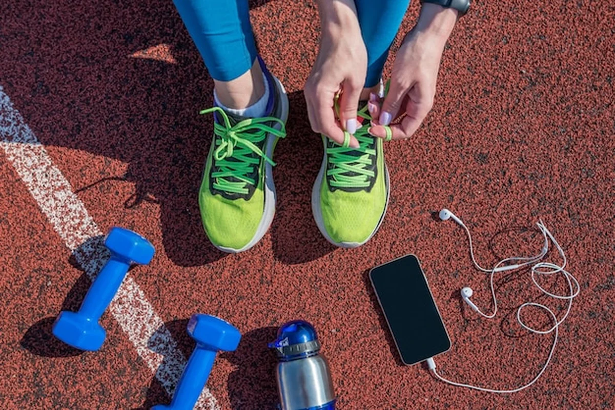 Biegaczka wiążąca sznurowadła na stadionowej bieżni z butelką wody i telefonem w słuchawkach, widok z góry